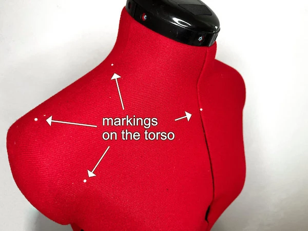Pins pinned to the various parts of the torso of a mannequin: shoulder beginning, shoulder tip, armscye centre and torso centre.