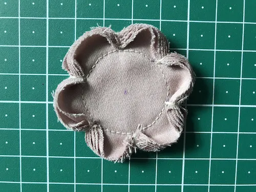 Circular fabric stack shaped by thread into flower.