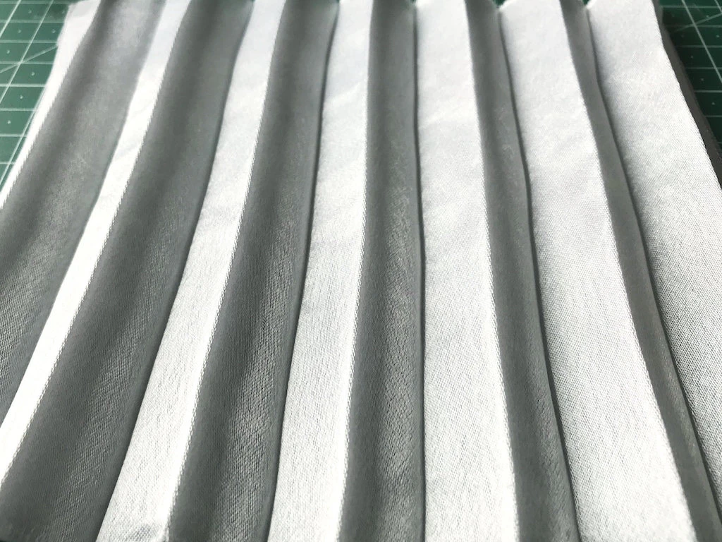 Creased permanently pleated crepe satin fabric. Permanent accordion pleats.