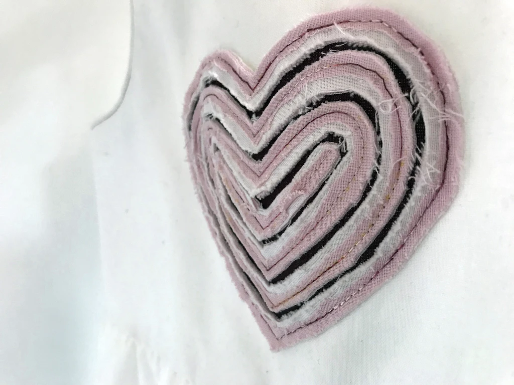 Pink faux chenille style applique sewn onto a white girls dress.