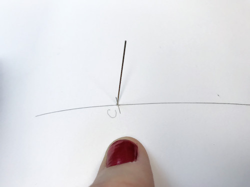 Sticking a pin through a paper to draw circular waist and hem of circle skirt pattern.