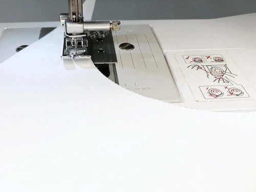 Sewing outer curved stitches on a sewing practice sheet.