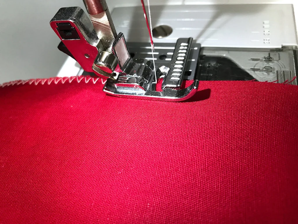 Finishing raw edges of fabric with a zig-zag stitch on a sewing machine.