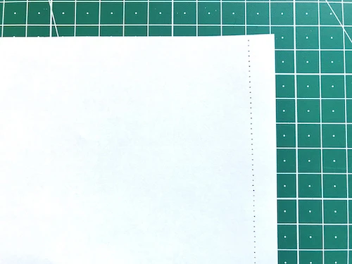 Sewing straight stitches along an edge of practice sewing paper.