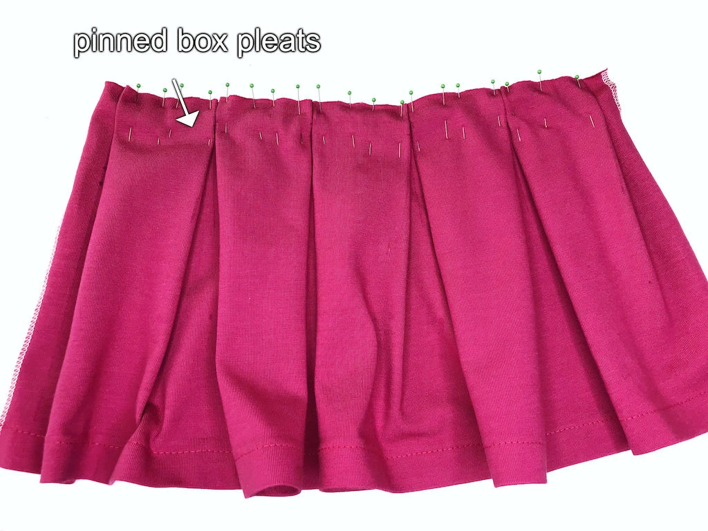 Pinned box pleats on pink knit jersey fabric.