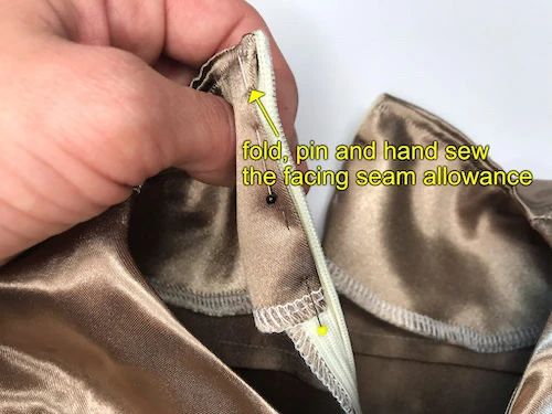Seam allowance of the neckline facing pinned to the concealed zipper of a beige satin dress.